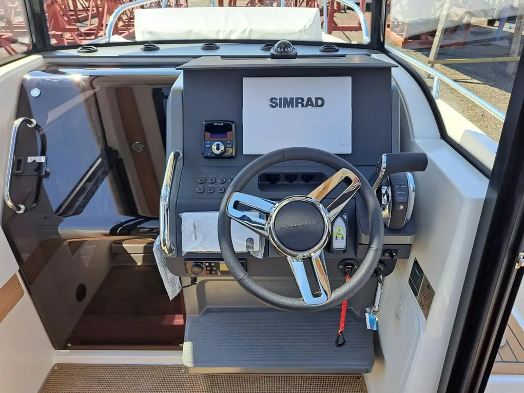Boat dashboard with a SIMRAD display, steering wheel, throttle control, and various navigation buttons on a sunny day.